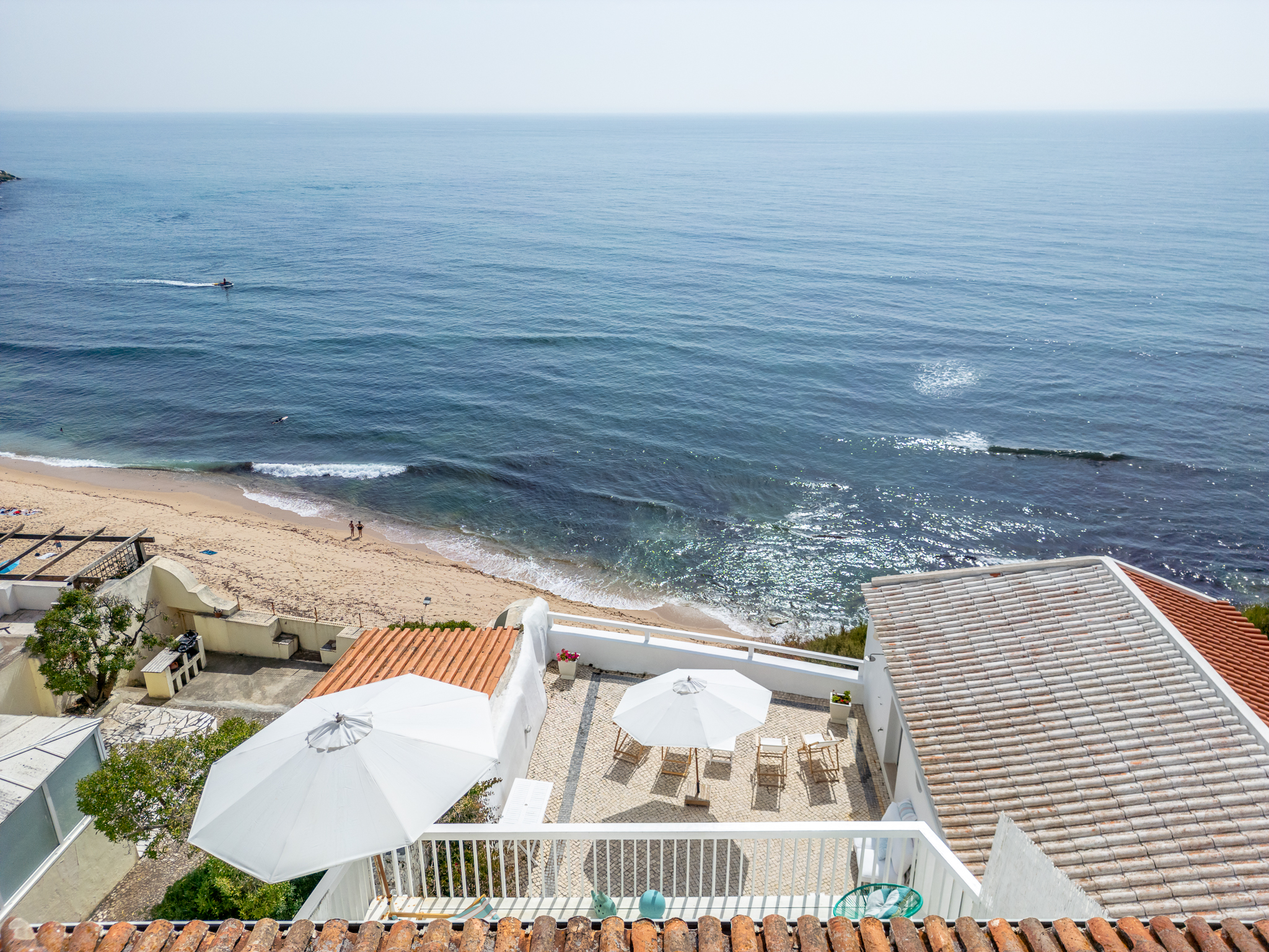 Vista aérea de terraço com guarda-sóis brancos sobre a praia da Ericeira — lifestyle costeiro