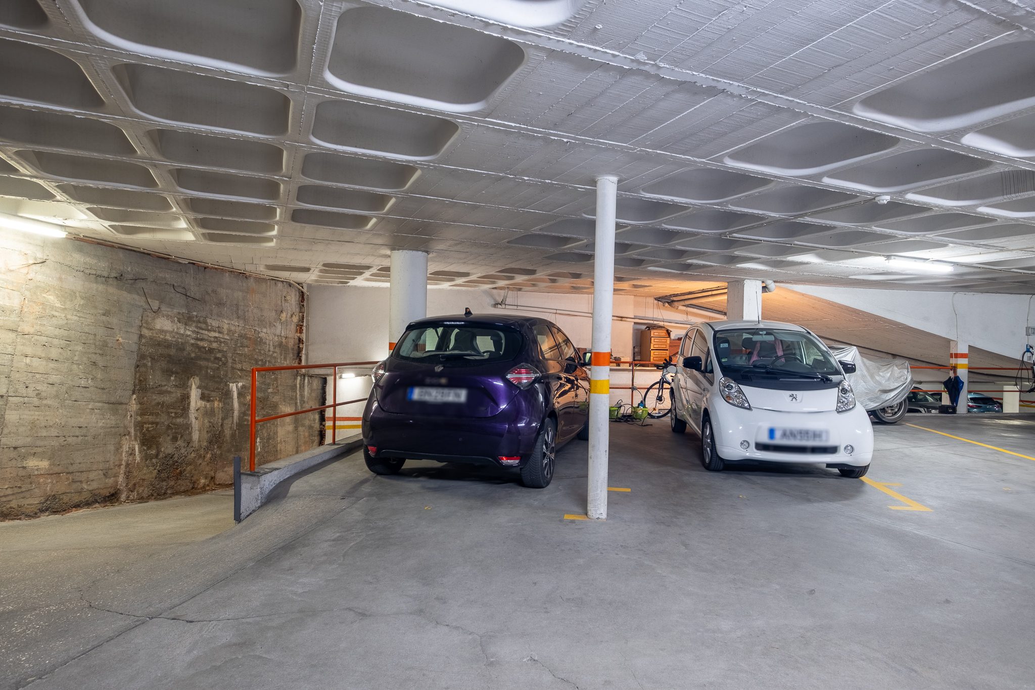 A garagem fechada em cave, no piso -1, com carros estacionados e a rampa de acesso