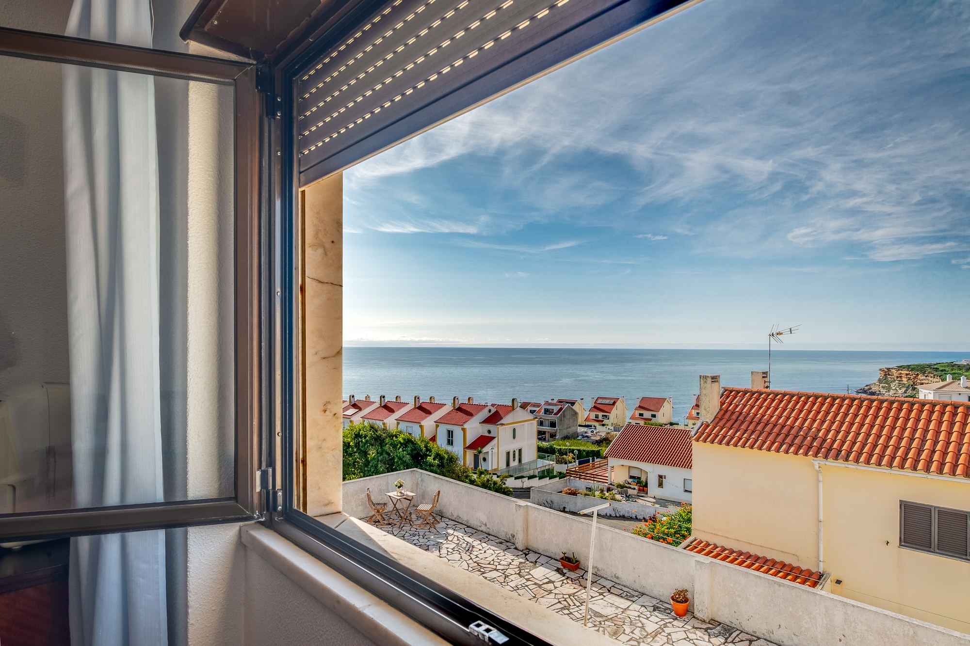 Janela aberta com vista sobre os telhados e o mar