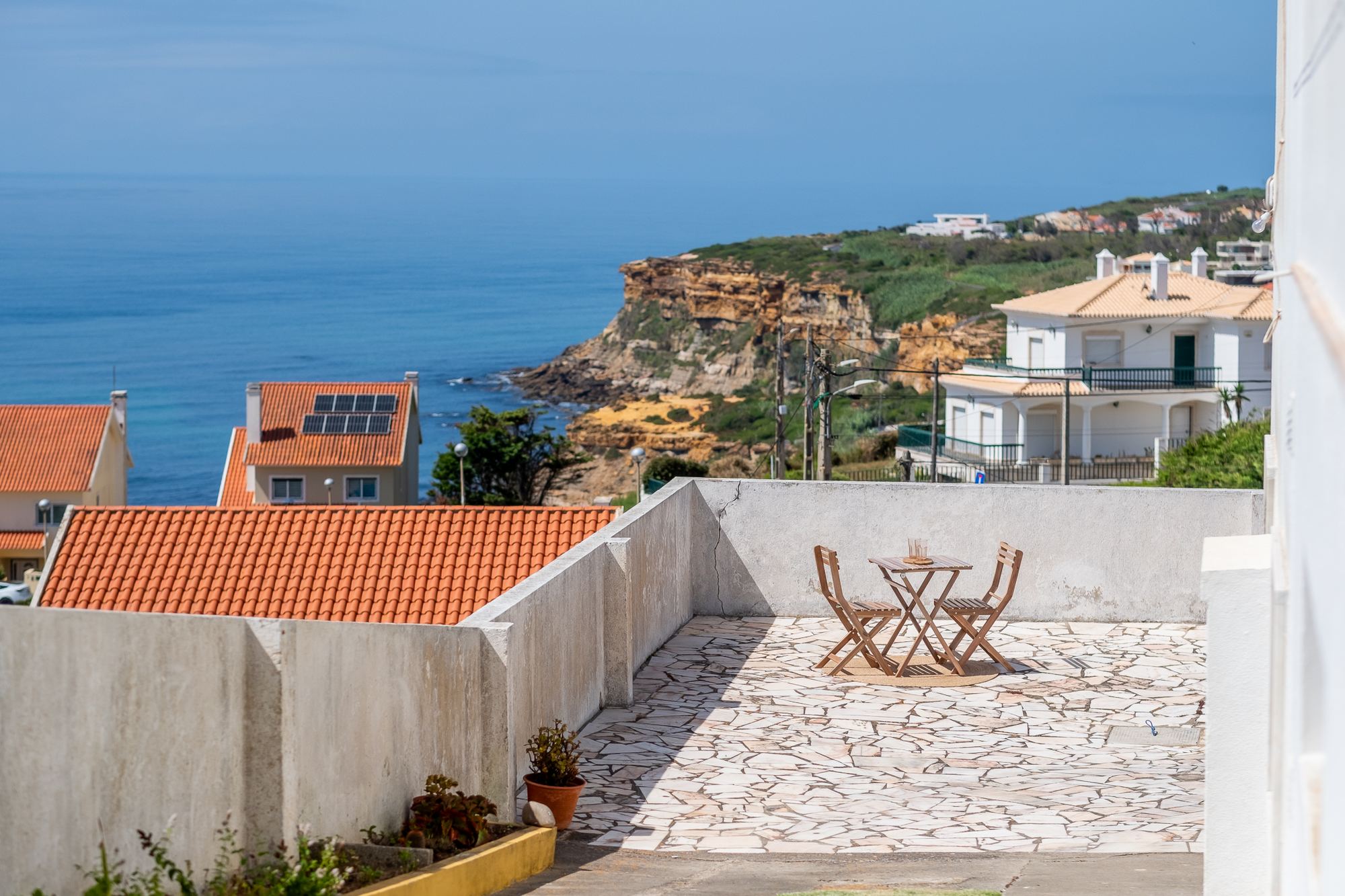 Terraço com mesa, cadeiras e vista sobre a arriba costeira