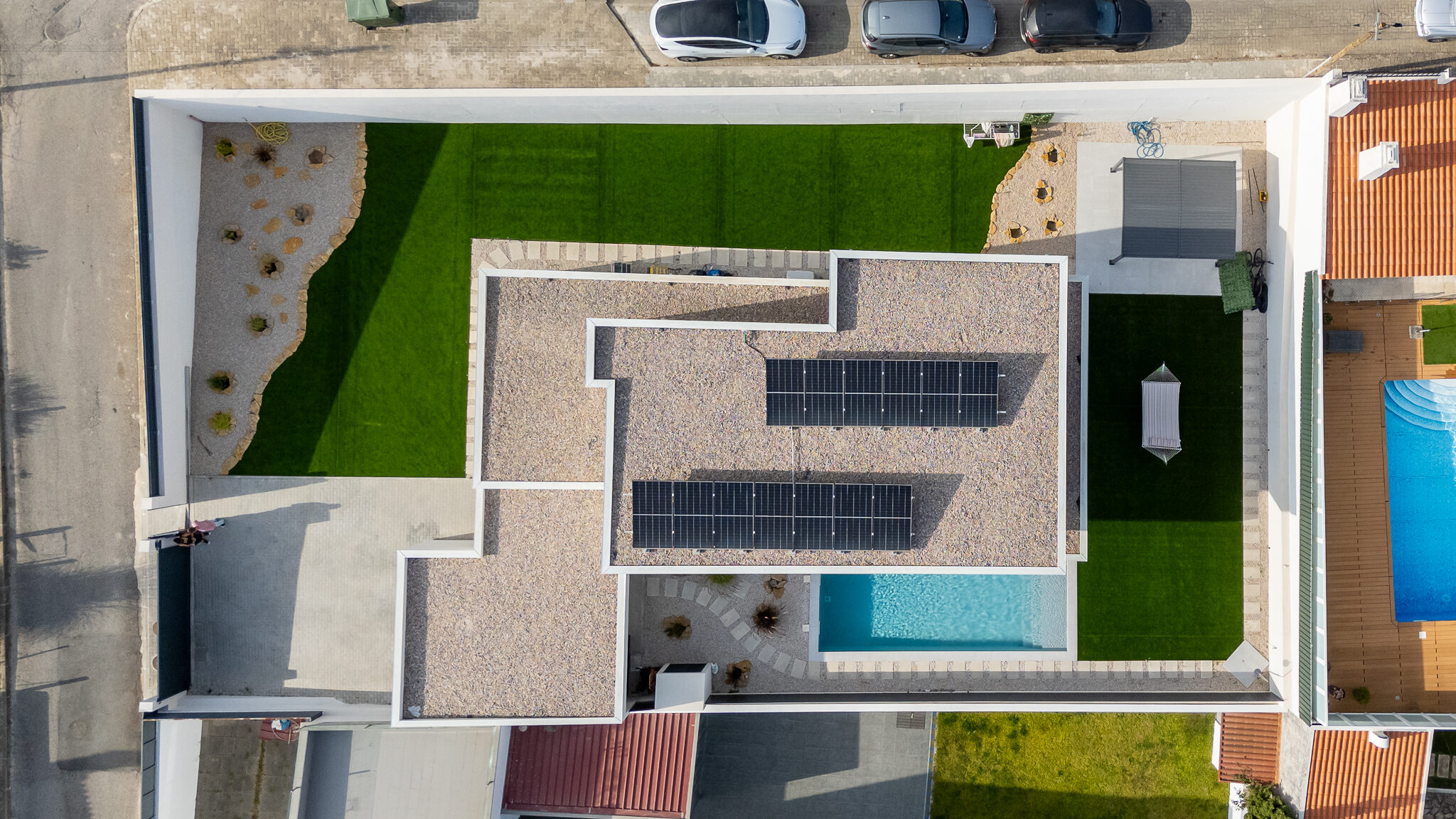 Vista aérea a pique da moradia, com os painéis fotovoltaicos no telhado, a piscina e o lote plano