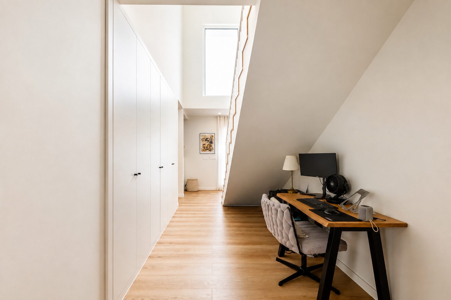 Hall com escada de pé-direito alto e zona de trabalho com secretária