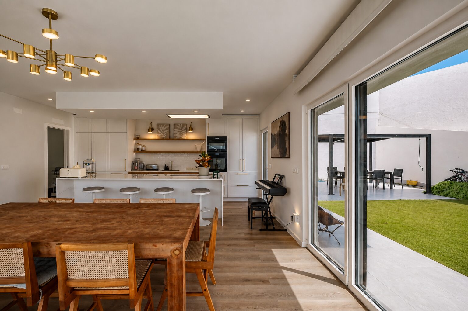 Mesa de jantar, ilha da cozinha e envidraçado de correr aberto para o relvado e a pérgola