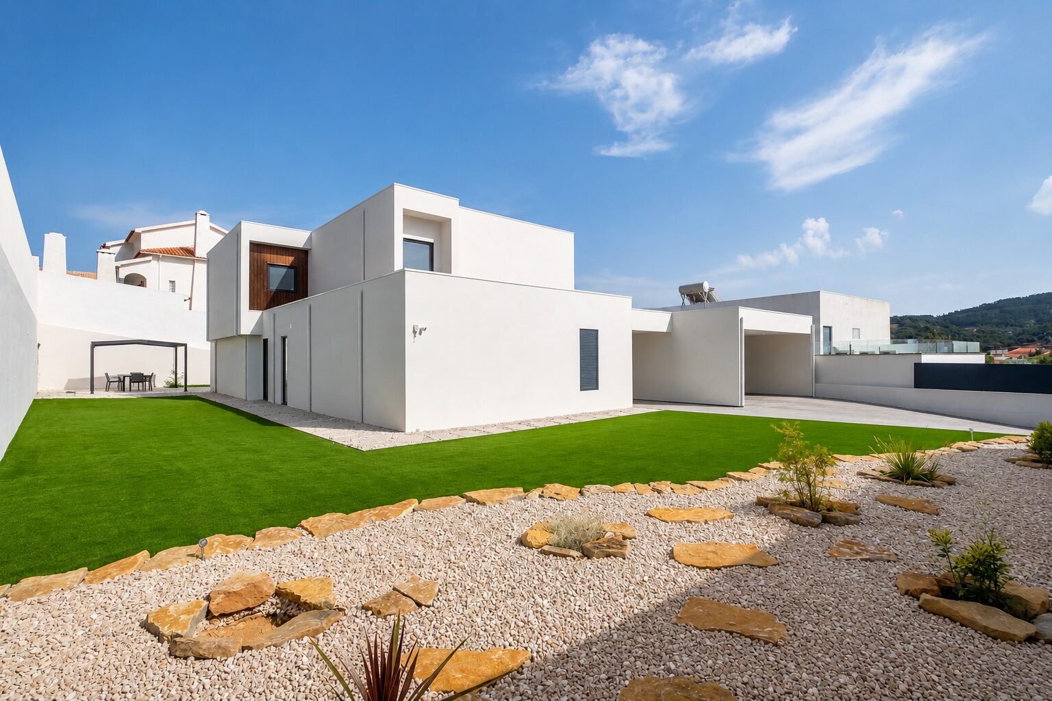 Jardim lateral com seixo, lajes de pedra e relvado junto aos volumes brancos