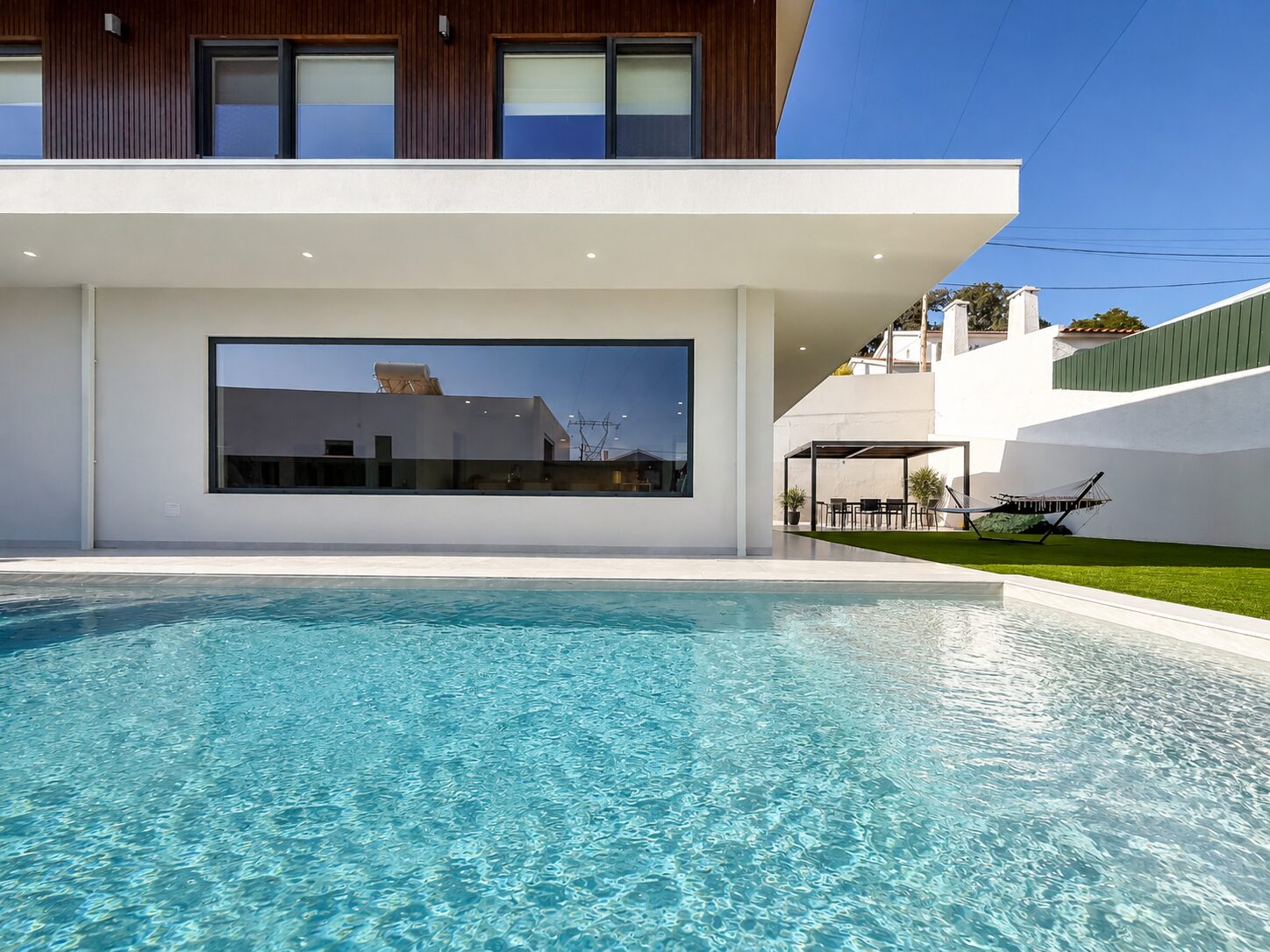 Piscina junto à fachada, com a pala do piso superior a sombrear o envidraçado