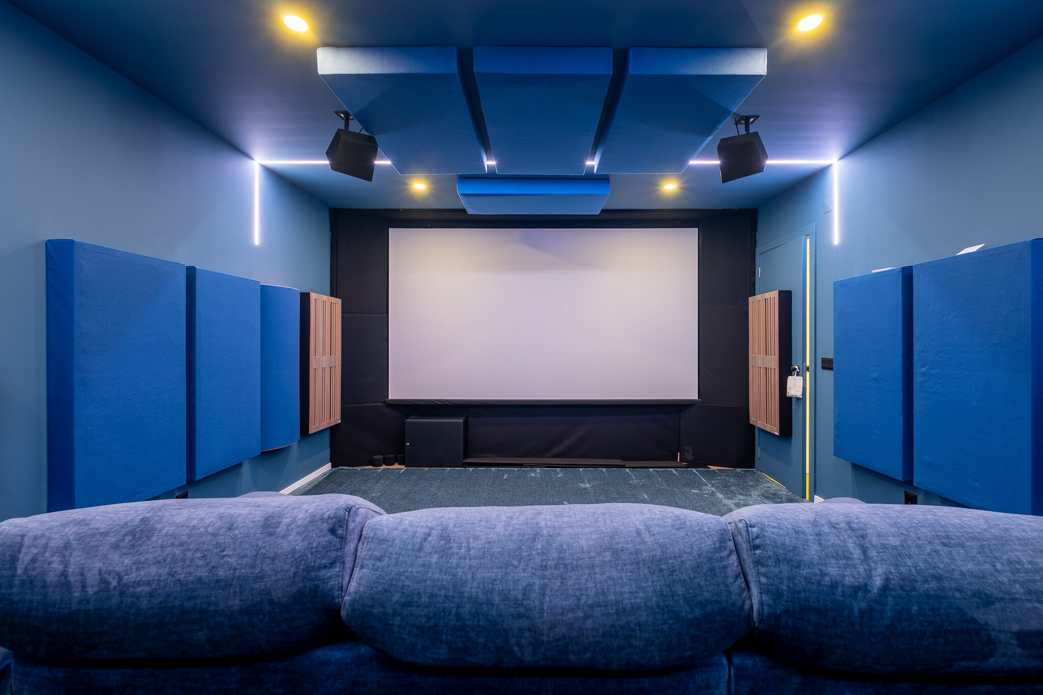 Sala de cinema com tela de projeção, painéis acústicos e sofá