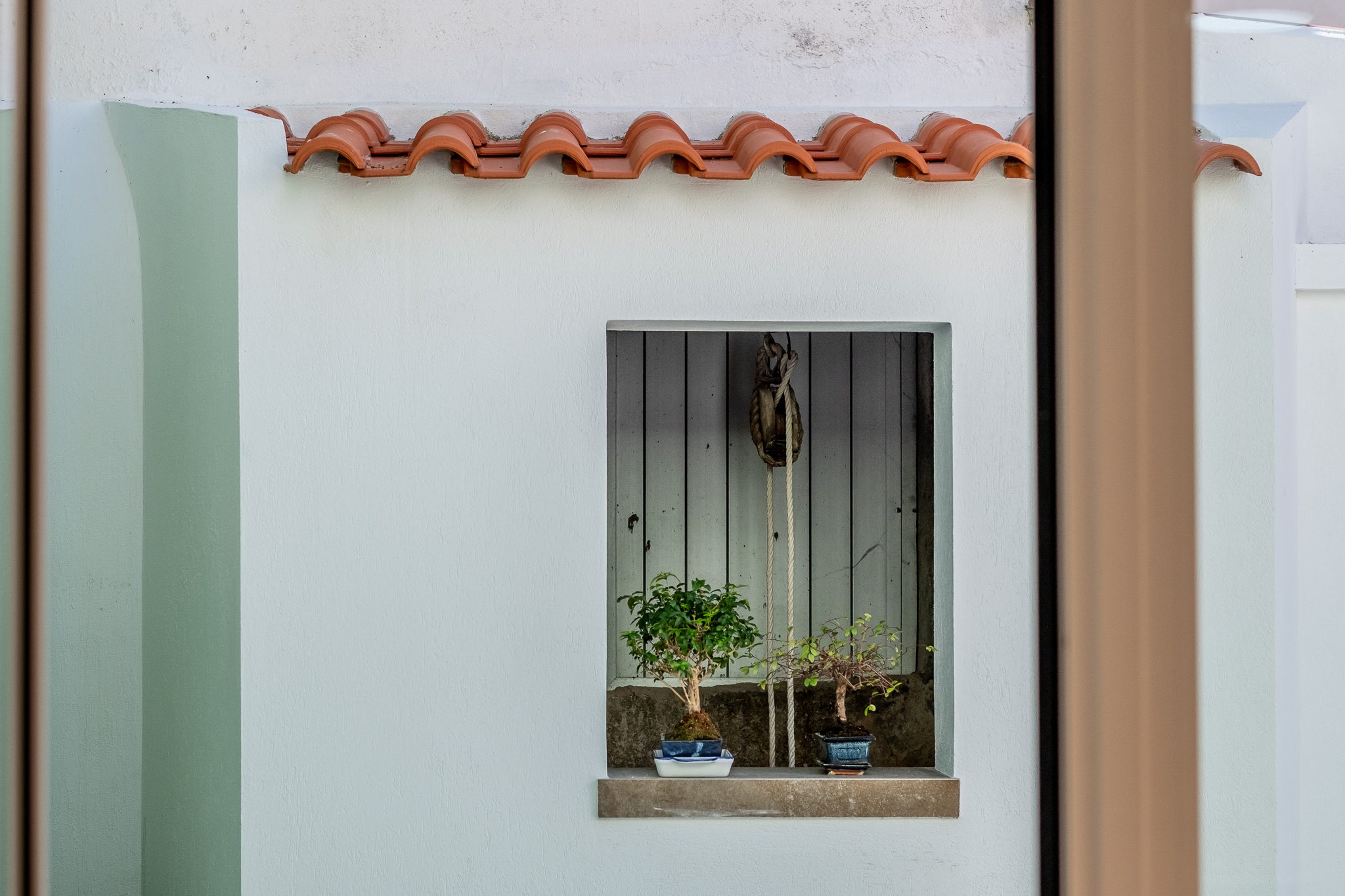 Roldana e corda originais do poço, preservadas no muro exterior com bonsais no parapeito