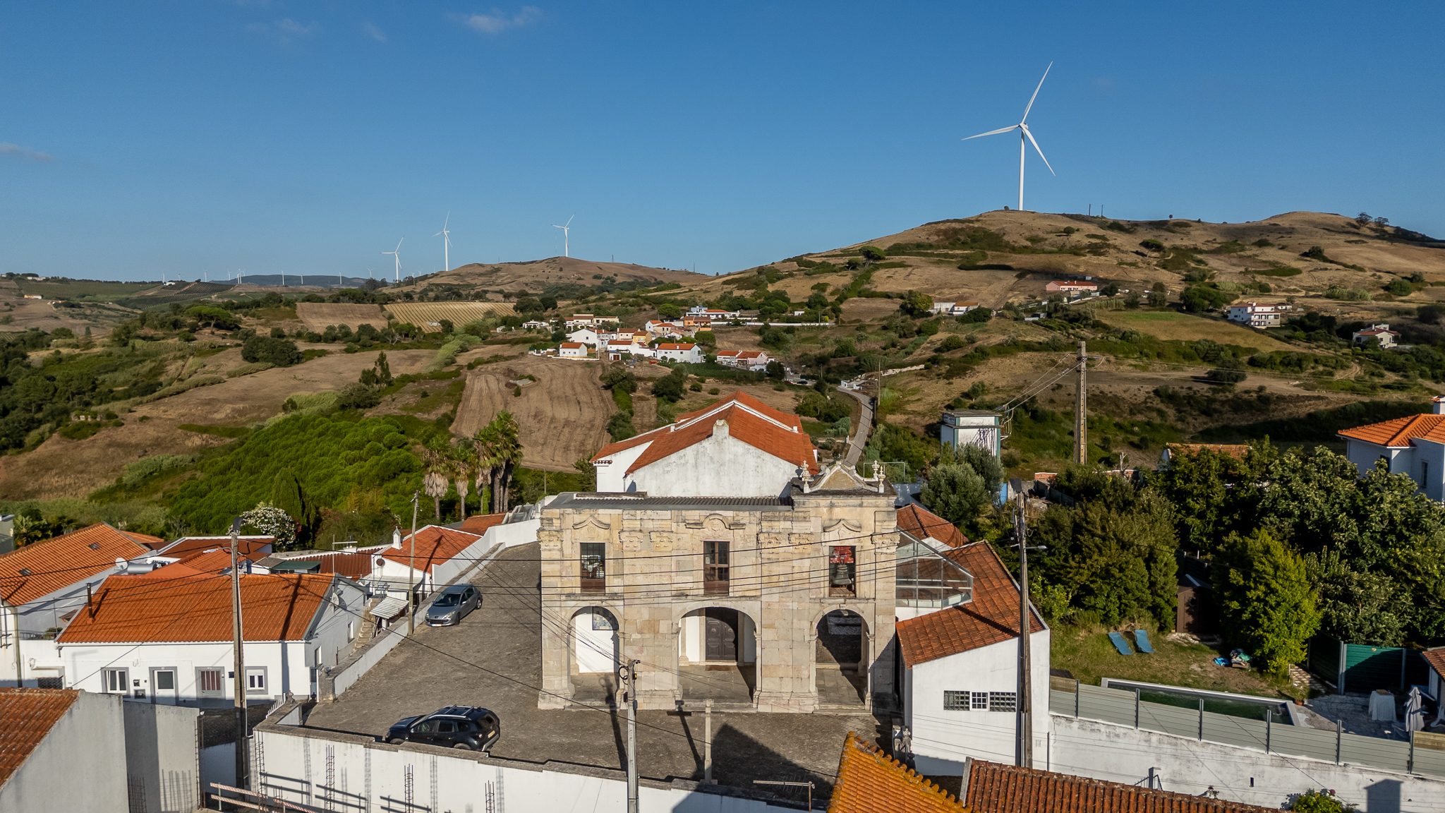 Igreja matriz de Vila Franca do Rosário, com a serra e os aerogeradores ao fundo