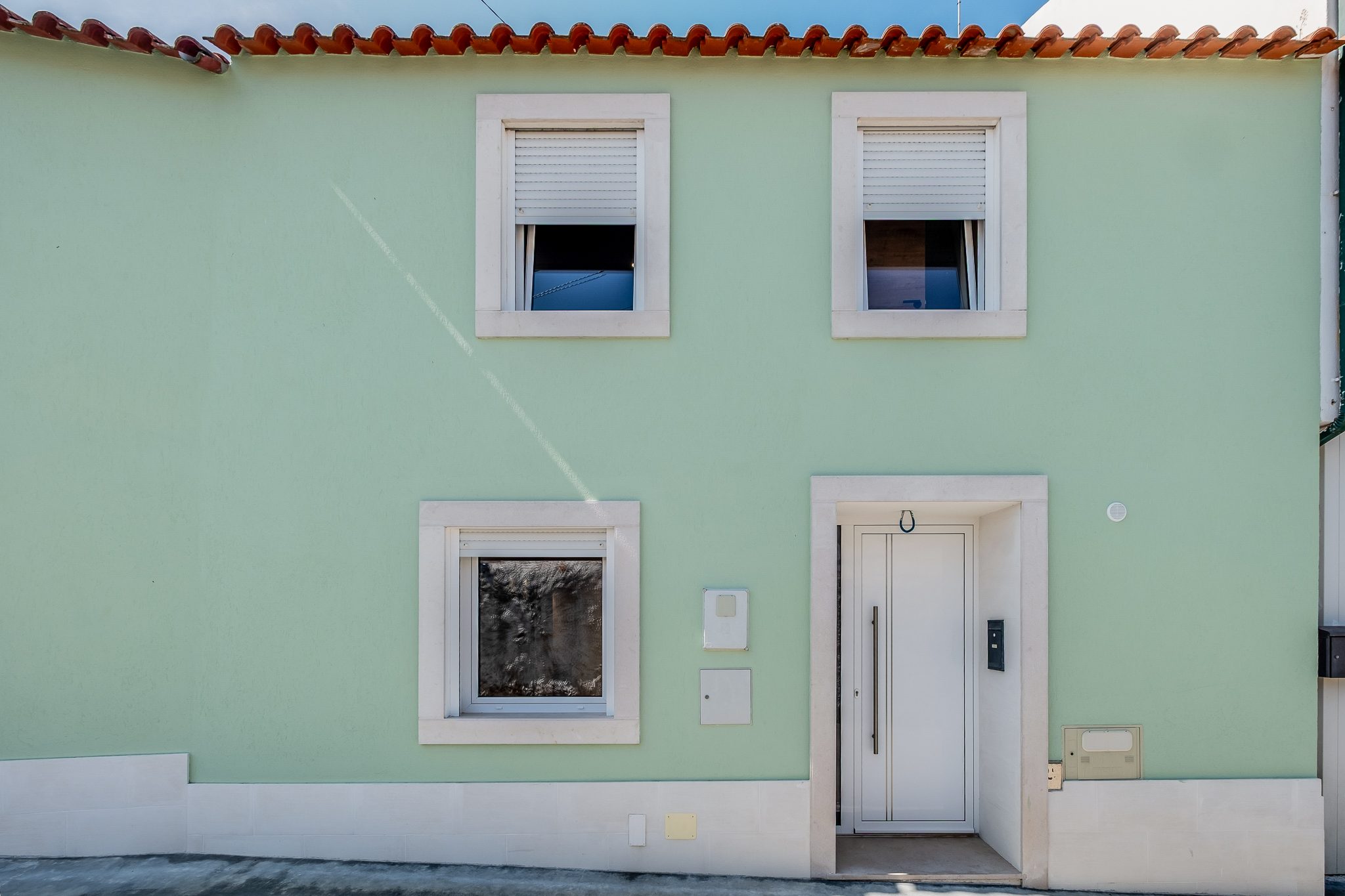 Fachada da moradia em verde-menta com cantarias em pedra e porta branca, na Rua Luís de Camões