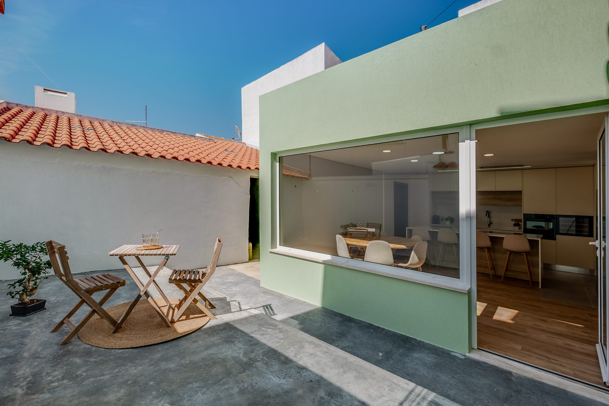 Pátio exterior com mesa e janelão corrido a abrir para a cozinha e sala de jantar