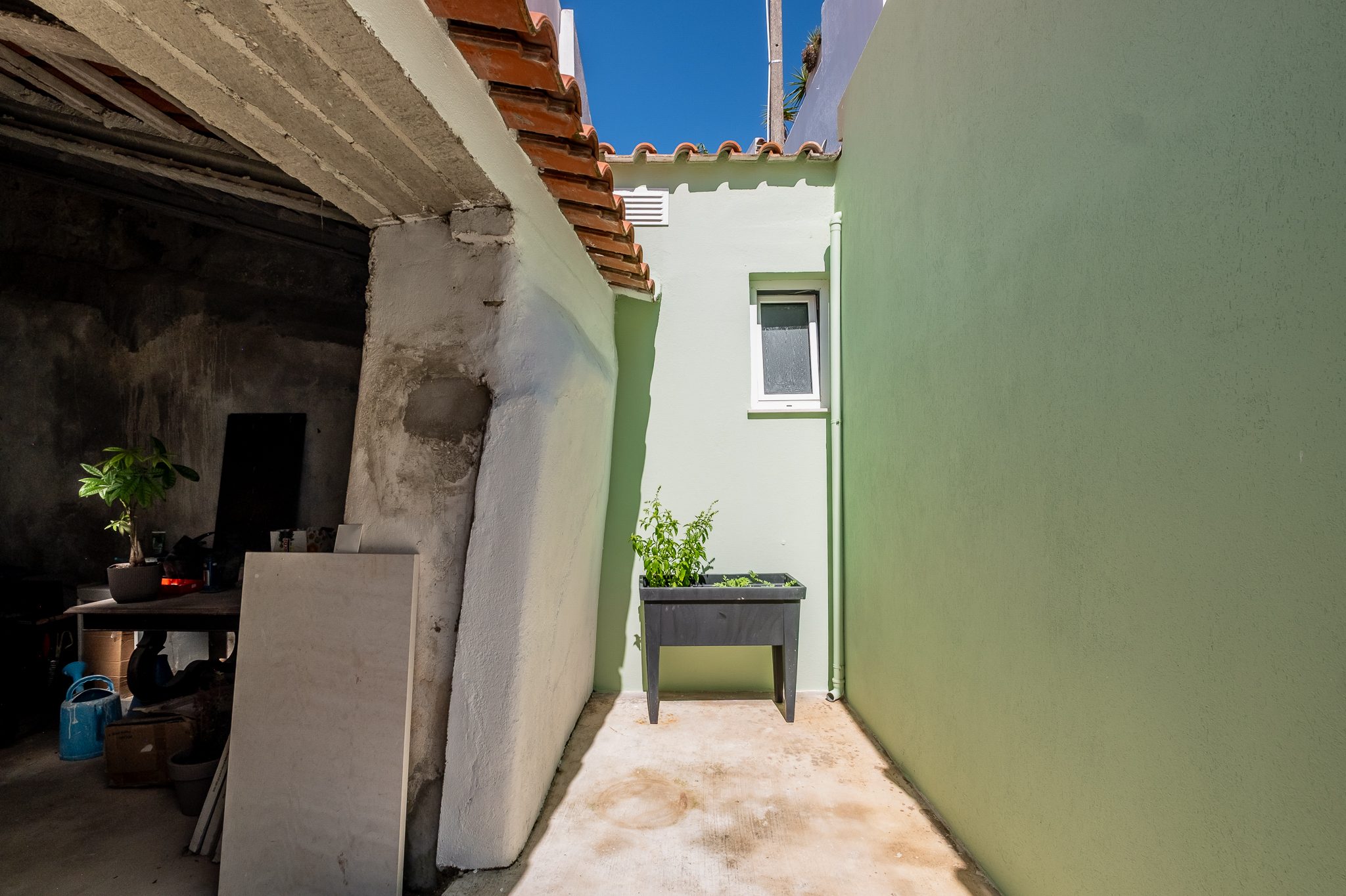 Passagem entre a parede da casa e a ruína, com canteiro de ervas aromáticas