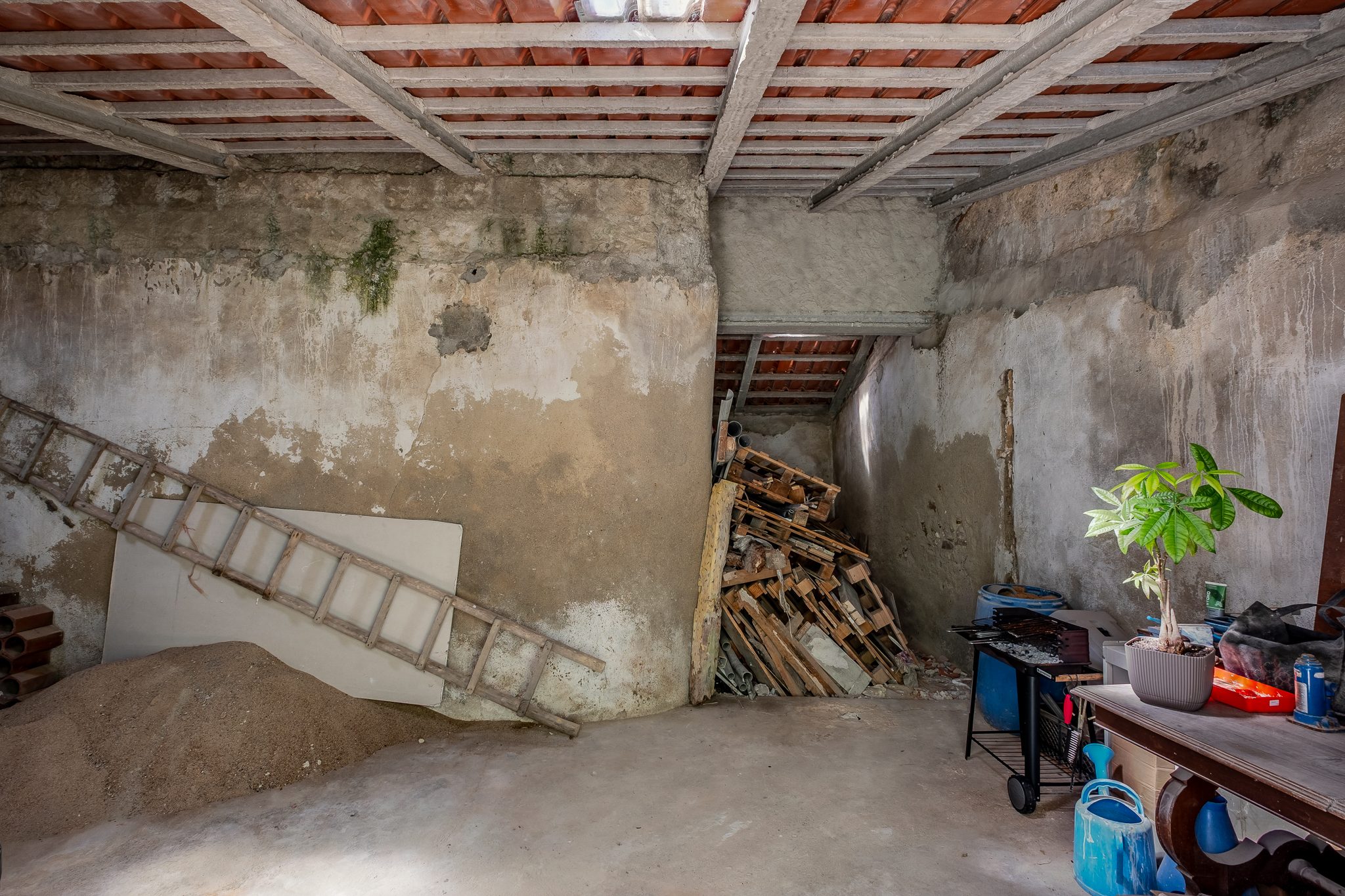 Interior da ruína com estrutura de vigotas e telha, escada antiga e materiais de obra